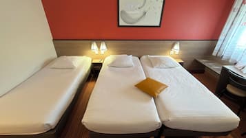 A hotel room with two single beds, a wooden floor, a red accent wall, and a framed abstract artwork.