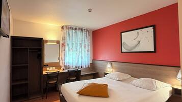 Habitación de hotel con cama, escritorio, silla y una pared de acento roja.