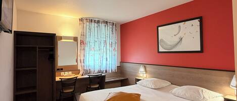 Quarto de hotel com cama, escrivaninha, cadeira e uma parede com detalhes em vermelho.