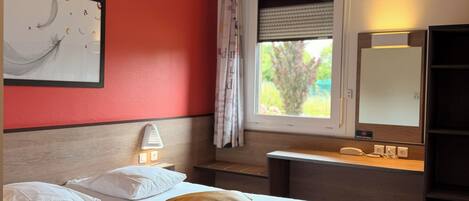 Habitación de hotel con cama, mesita de noche, lámpara, ventana con persianas y espejo.