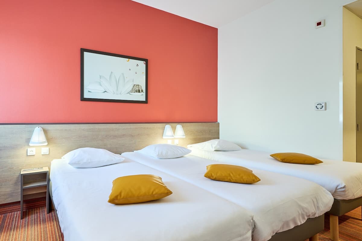 A hotel room with a red accent wall, a framed picture, two bedside lamps, a bed with white bedding and yellow pillows, a wooden nightstand, and a carpeted floor.