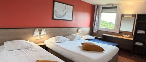 A hotel room with two beds, a red accent wall, a framed artwork, a window with curtains, and a desk with a lamp.