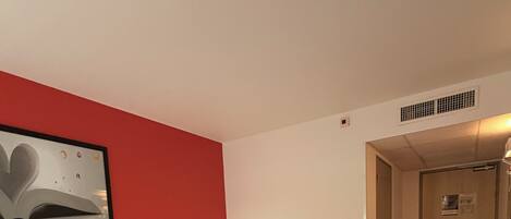 Una habitación de hotel con dos camas, una pared de acento roja, un cuadro enmarcado y suelo de madera.