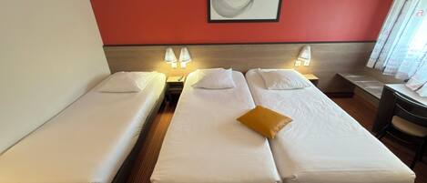 A hotel room with two single beds, a wooden headboard, a framed abstract artwork on the wall, and a desk with a chair.