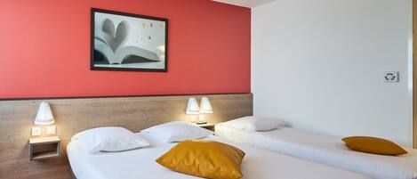 A hotel room with two beds, a red accent wall, a framed picture, bedside lamps, and a striped carpet.