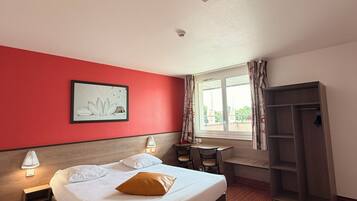A hotel room with a bed, a desk, a chair, a wardrobe, and a window with curtains.