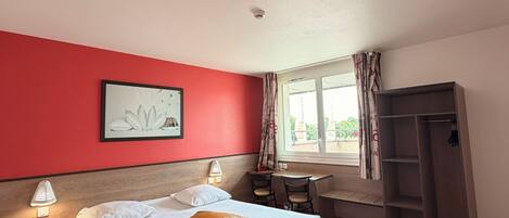 Ein Hotelzimmer mit Bett, Schreibtisch, Stuhl, Kleiderschrank und einem Fenster mit Vorhängen.