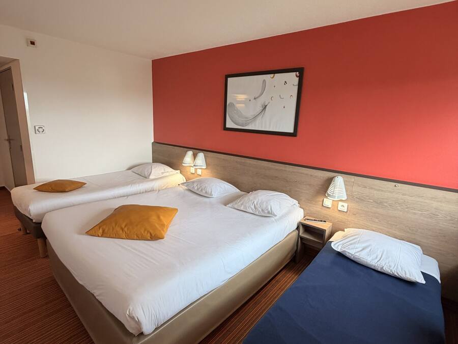 A hotel room with two beds, a red accent wall, a framed artwork, and a ceiling light.