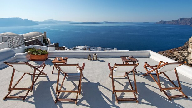 Una terraza con sillas y mesa de madera, con vista a un mar azul y cristalino y a islas en la distancia.