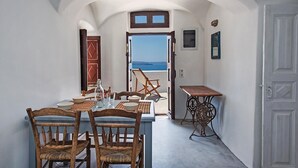 Un comedor con una mesa dispuesta para cuatro, vista al mar a través de un arco abierto y una pequeña mesa con base decorativa.