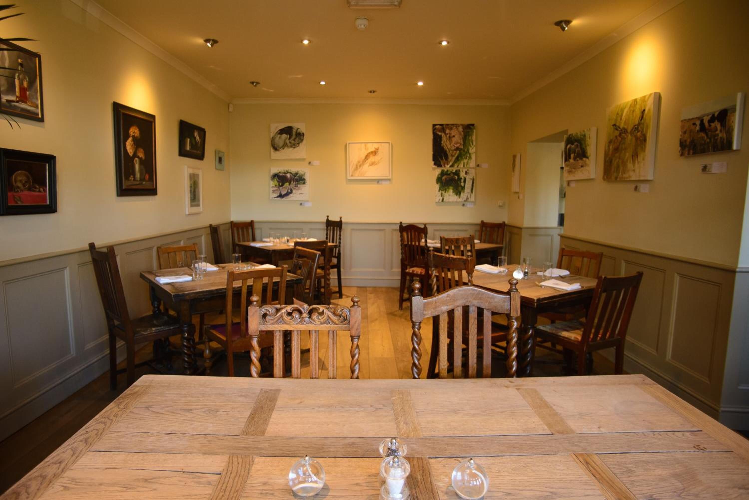 Un comedor con mesas y sillas de madera, obras de arte enmarcadas en las paredes y una araña.