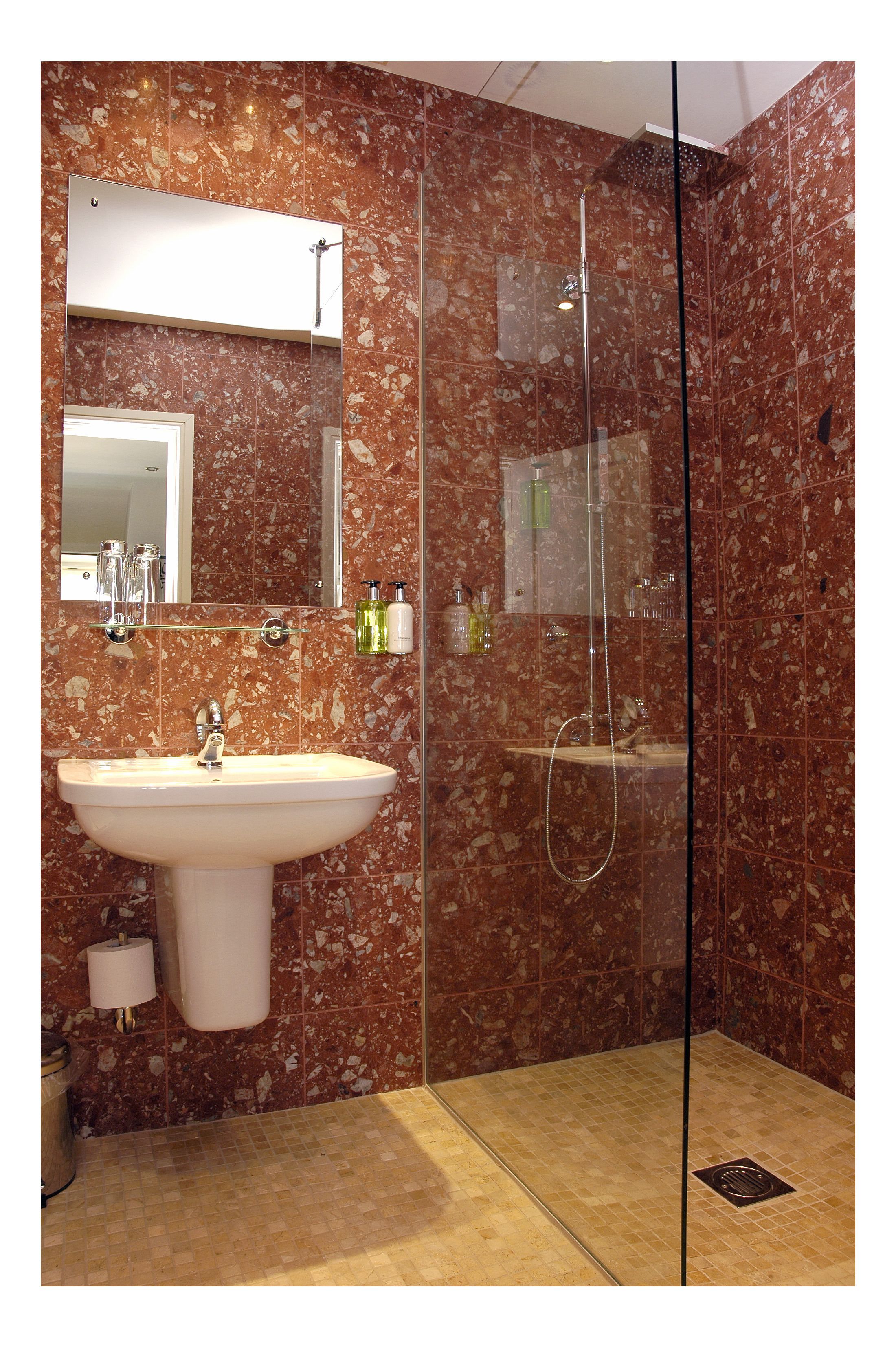 Un baño con pared de mármol, un lavabo, un espejo y cabina de ducha con mampara de vidrio.