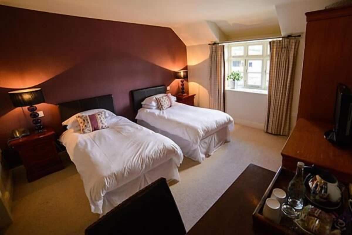 A hotel room with two beds, a desk, a TV, and a window with curtains.