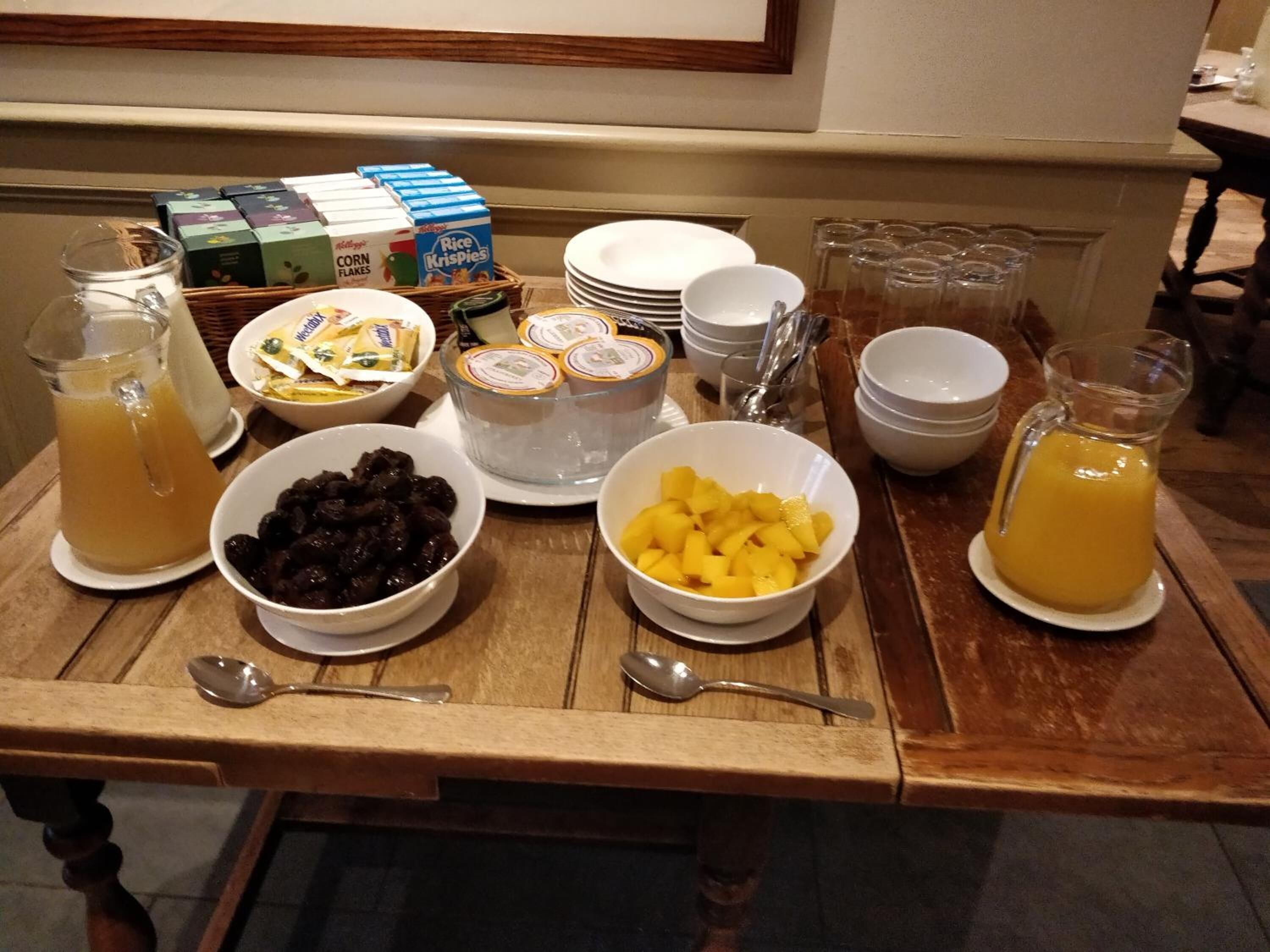 Una mesa de desayuno buffet con diversos alimentos, como cajas de cereales, frutas y bebidas.