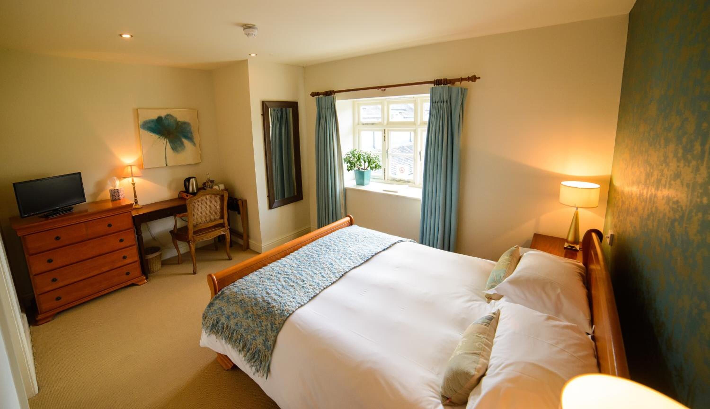 A bedroom with a bed, a desk, a chair, a television, and a window with curtains.