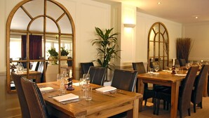 A dining area with wooden tables and chairs, large mirrors, and a potted plant. - The Kings Arms (Sherborne)