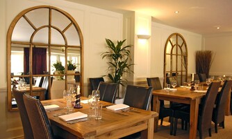Un comedor con mesas y sillas de madera, espejos grandes y una planta en maceta.