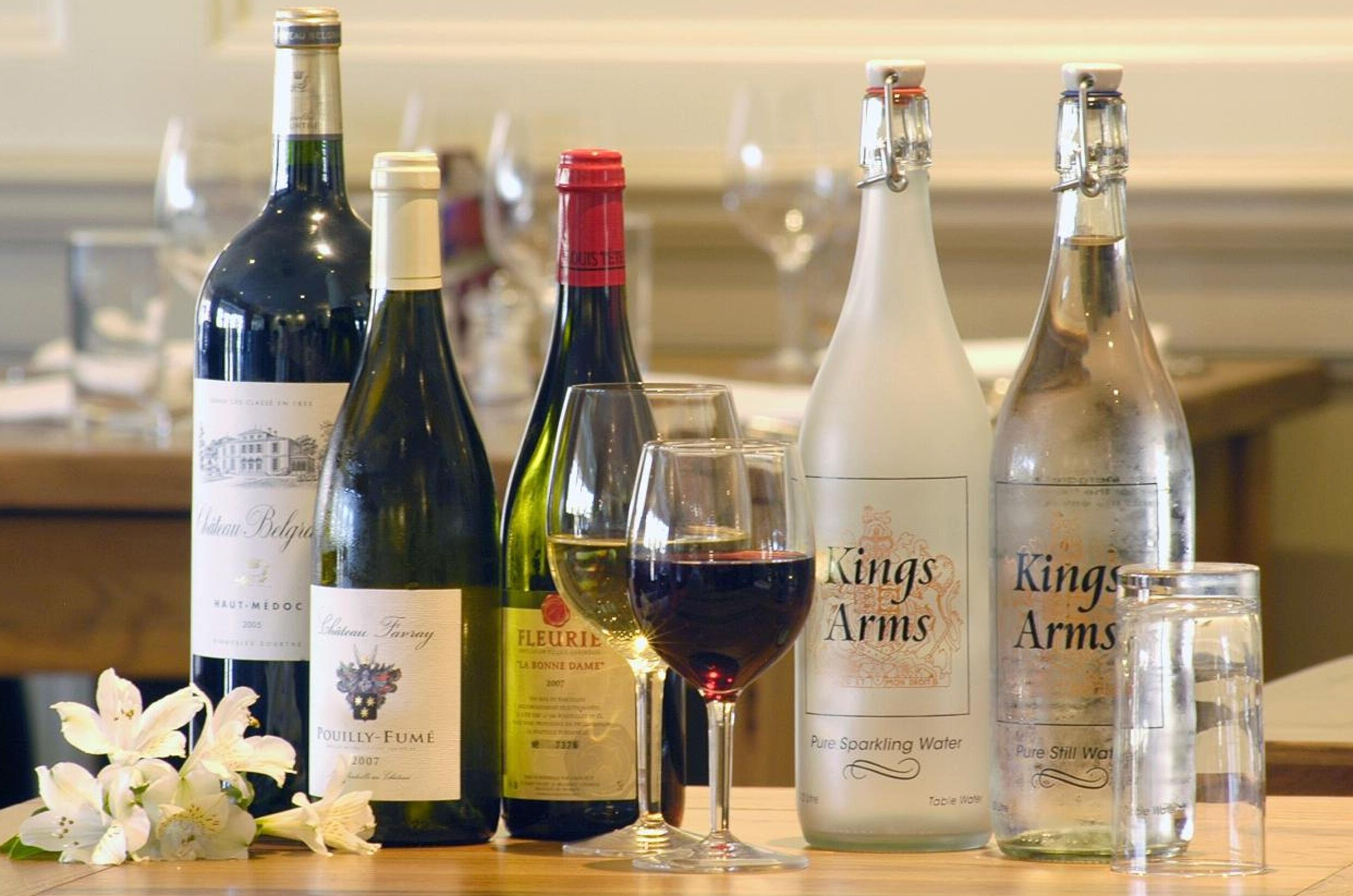 Différentes bouteilles de vin et d’eau gazeuse sont posées sur une table, à côté d’un verre de vin rouge.