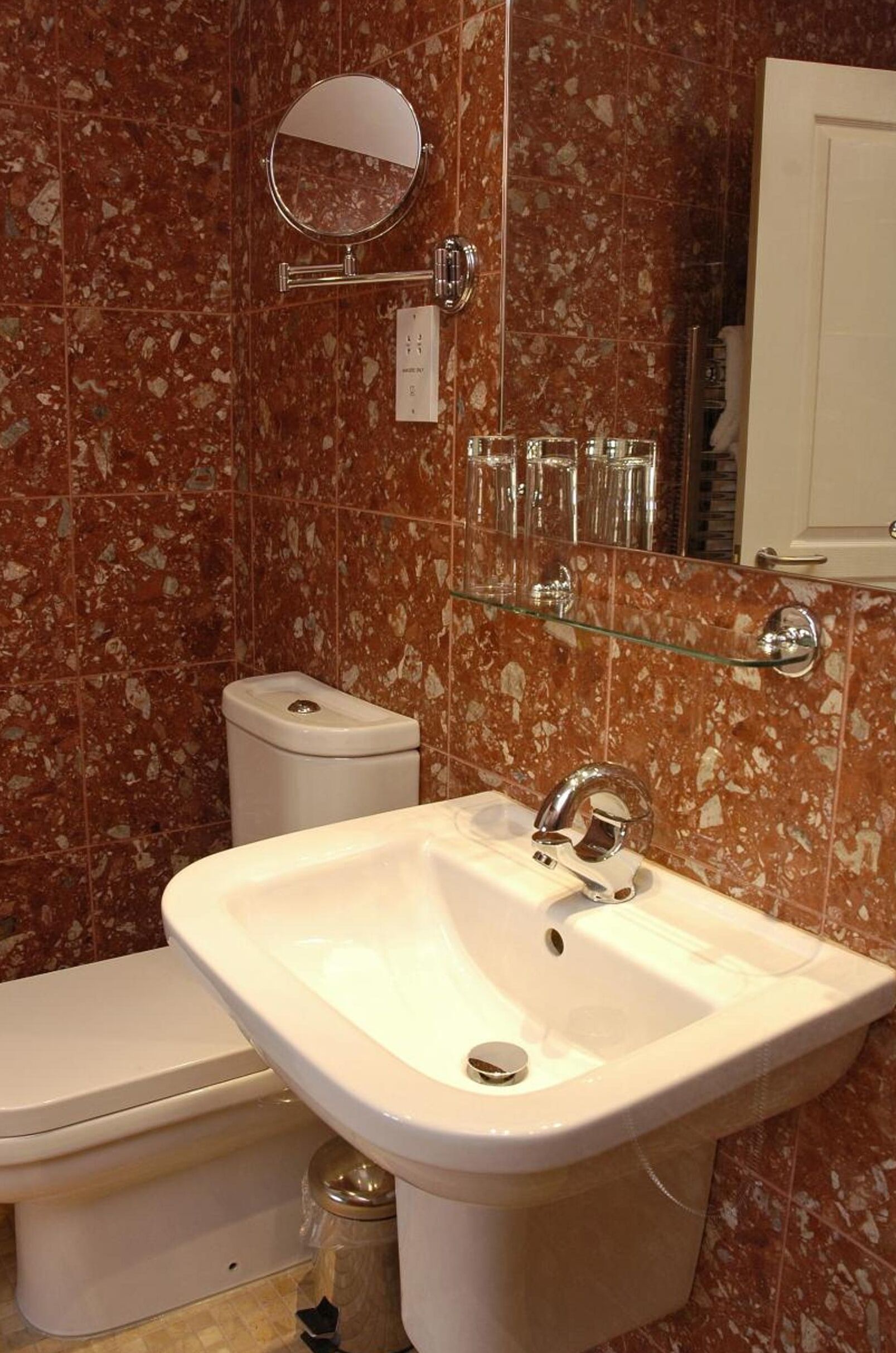 Une salle de bain avec un lavabo blanc, un miroir et des toilettes. On peut voir des récipients en verre sur une étagère au-dessus du lavabo.