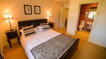 Habitación de hotel con una cama grande, dos mesitas de noche con lámparas, una puerta al baño e impresiones botánicas enmarcadas en la pared.