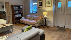 A cozy living room with a sofa, a coffee table, a bookshelf, and a lamp. - The Kings Arms (Sherborne)