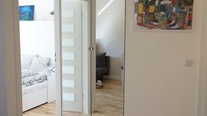 Huoneessa on puulattia, kuviollinen peitto sängyllä, valkoinen ovi ja värikäs abstrakti maalaus seinällä.