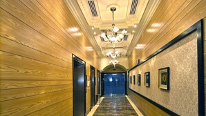 A hallway with wooden paneling, a chandelier, and framed pictures on the walls. - Alain Hotel Ajman (Ajman)