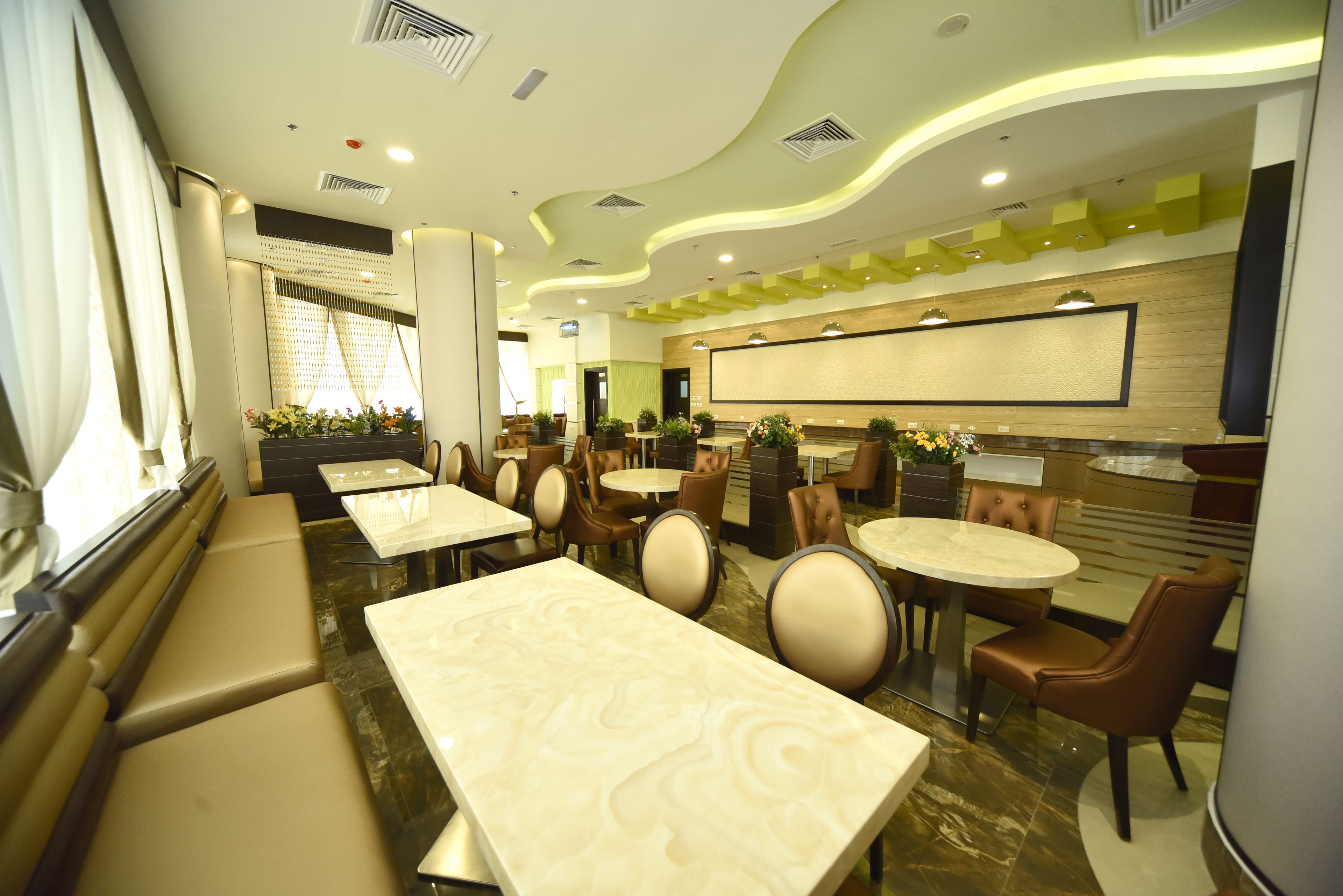 Restaurante moderno com mesas de mármore e cadeiras estofadas, uma tela grande e um design de teto verde.