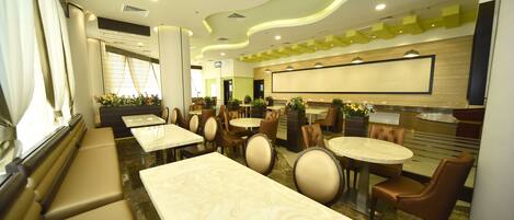 Un restaurante moderno con mesas de mármol y sillas acolchadas, una pantalla grande y un diseño de techo verde.