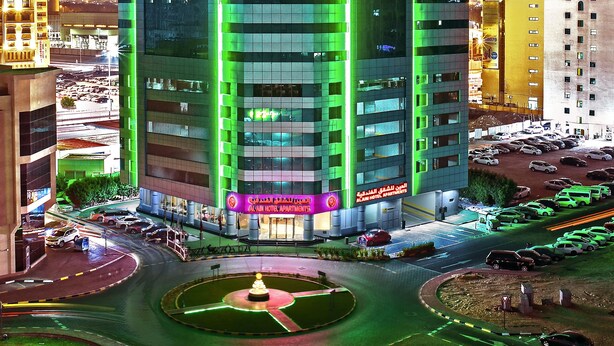 A multi-story building with a modern design, featuring a prominent entrance and a parking area in front. - Alain Hotel Ajman (Ajman)