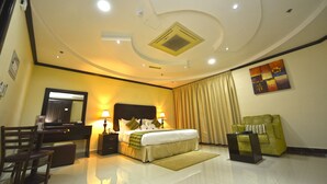 A hotel room with a bed, bedside tables, a desk, a chair, a green armchair, and a large mirror. - Alain Hotel Ajman (Ajman)