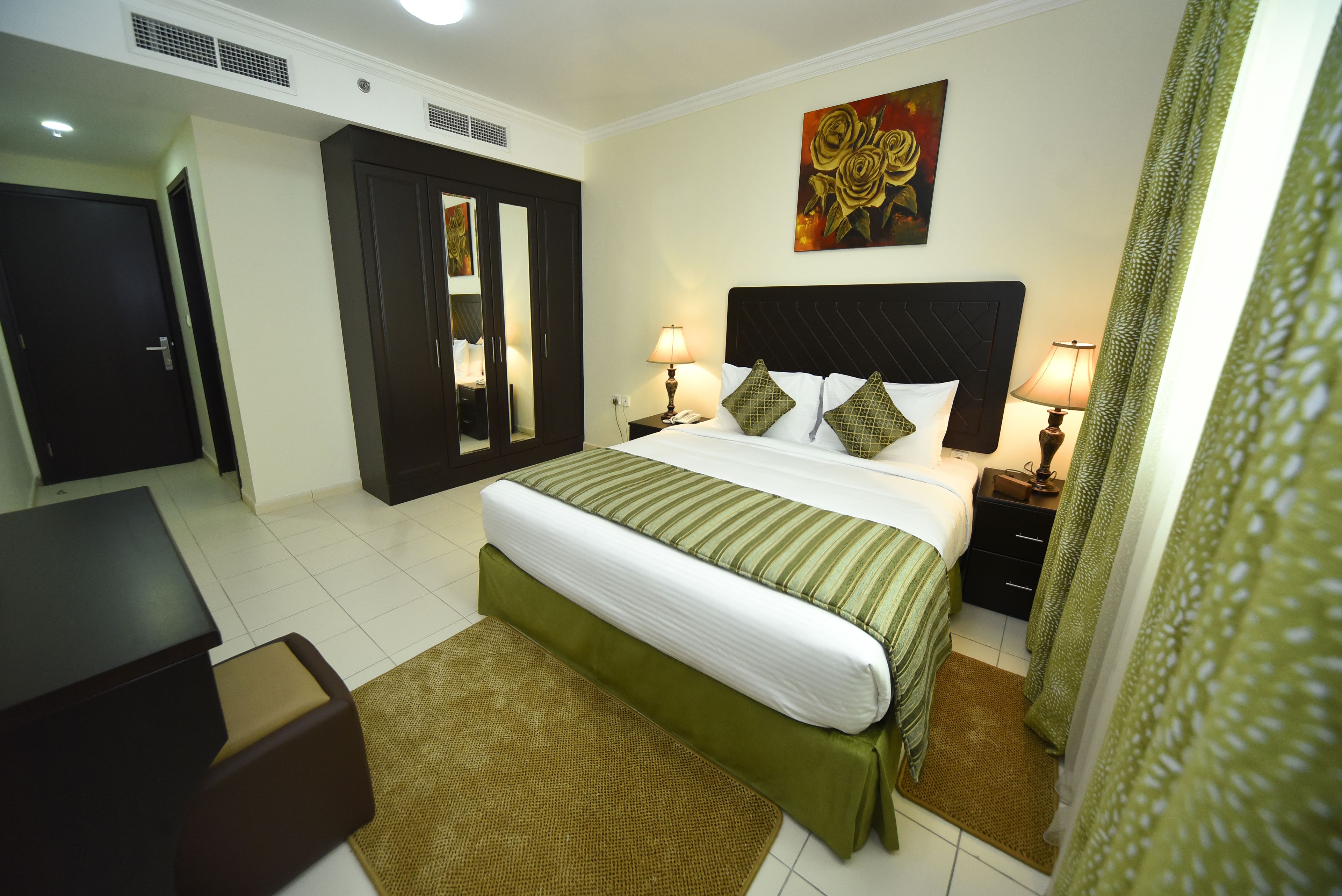 Una habitación de hotel con cama, mesitas de noche, escritorio, espejo y un cuadro en la pared.