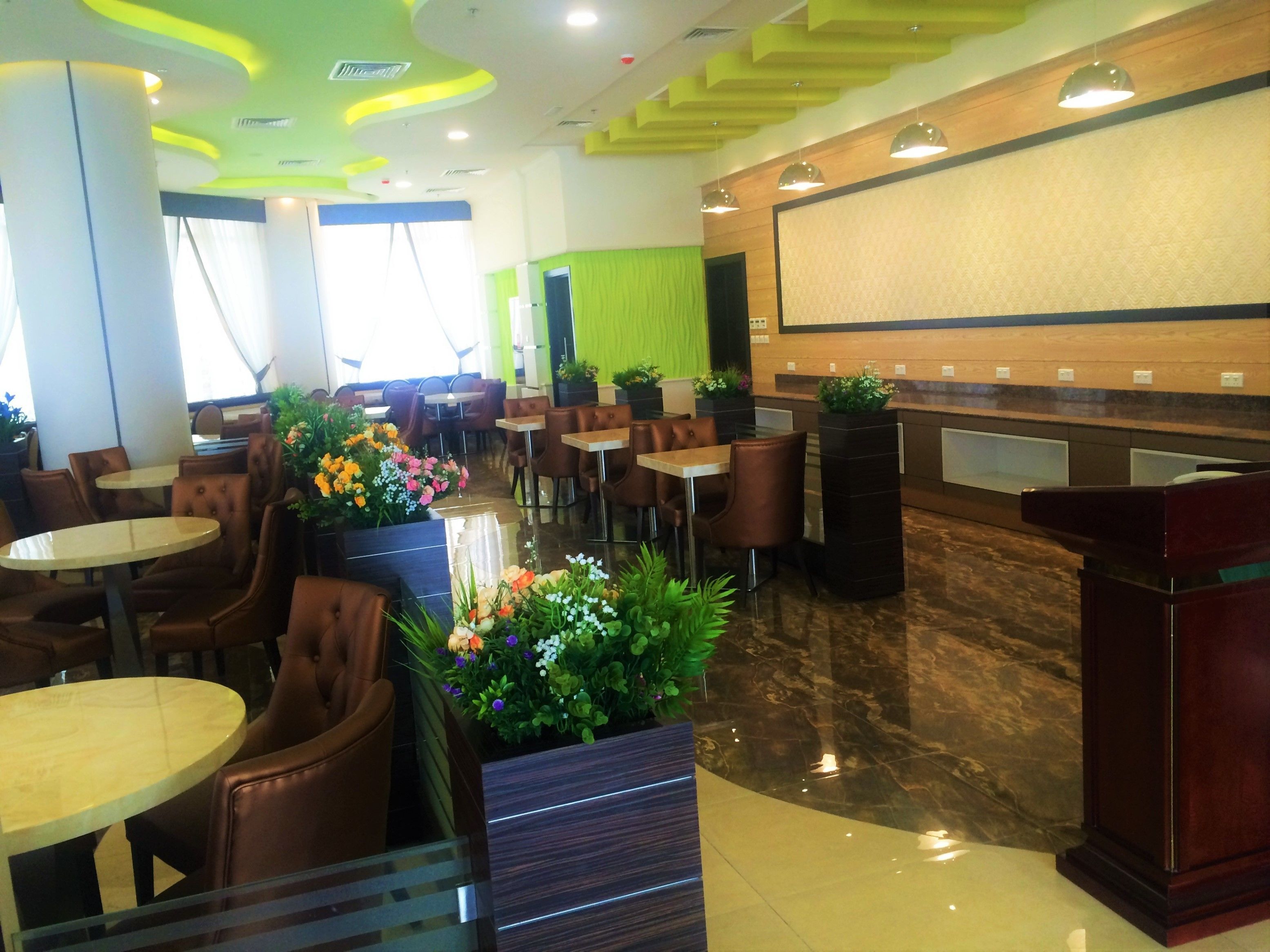 Un restaurante moderno con mesas redondas y cabinas, una zona de recepción e instalaciones con plantas decorativas.