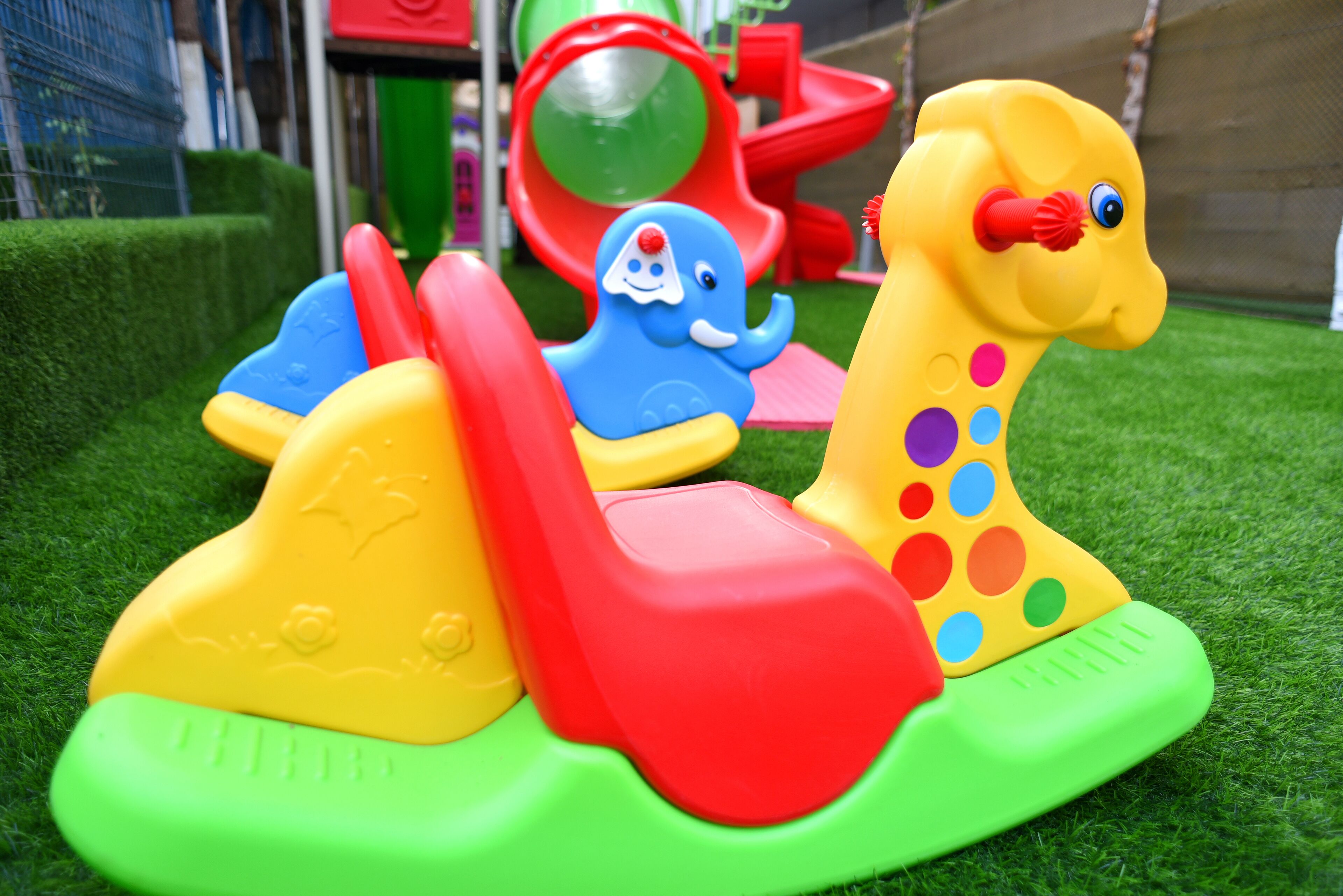 Ein Kinderspielbereich mit bunten Plastikspielzeugen, darunter ein gelber und ein blauer Elefant, auf künstlichem Rasen.
