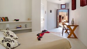 A bedroom with a bed, a desk, a chair, a bookshelf, and a door leading to another room. - Villa Amalia (Santorini)