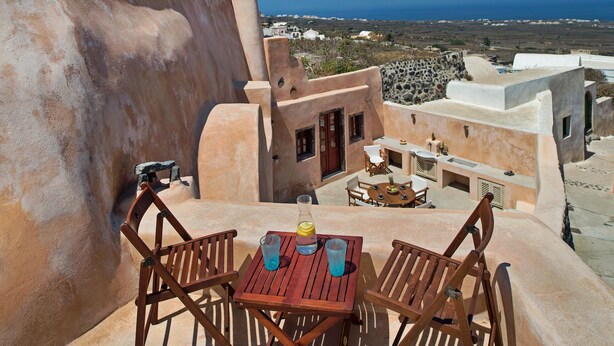A wooden table with two chairs on a rooftop terrace with a view of the sea and buildings in the background. - Villa Amalia (Santorini)
