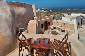 A wooden table with two chairs on a rooftop terrace with a view of the sea and buildings in the background. - Villa Amalia (Santorini)