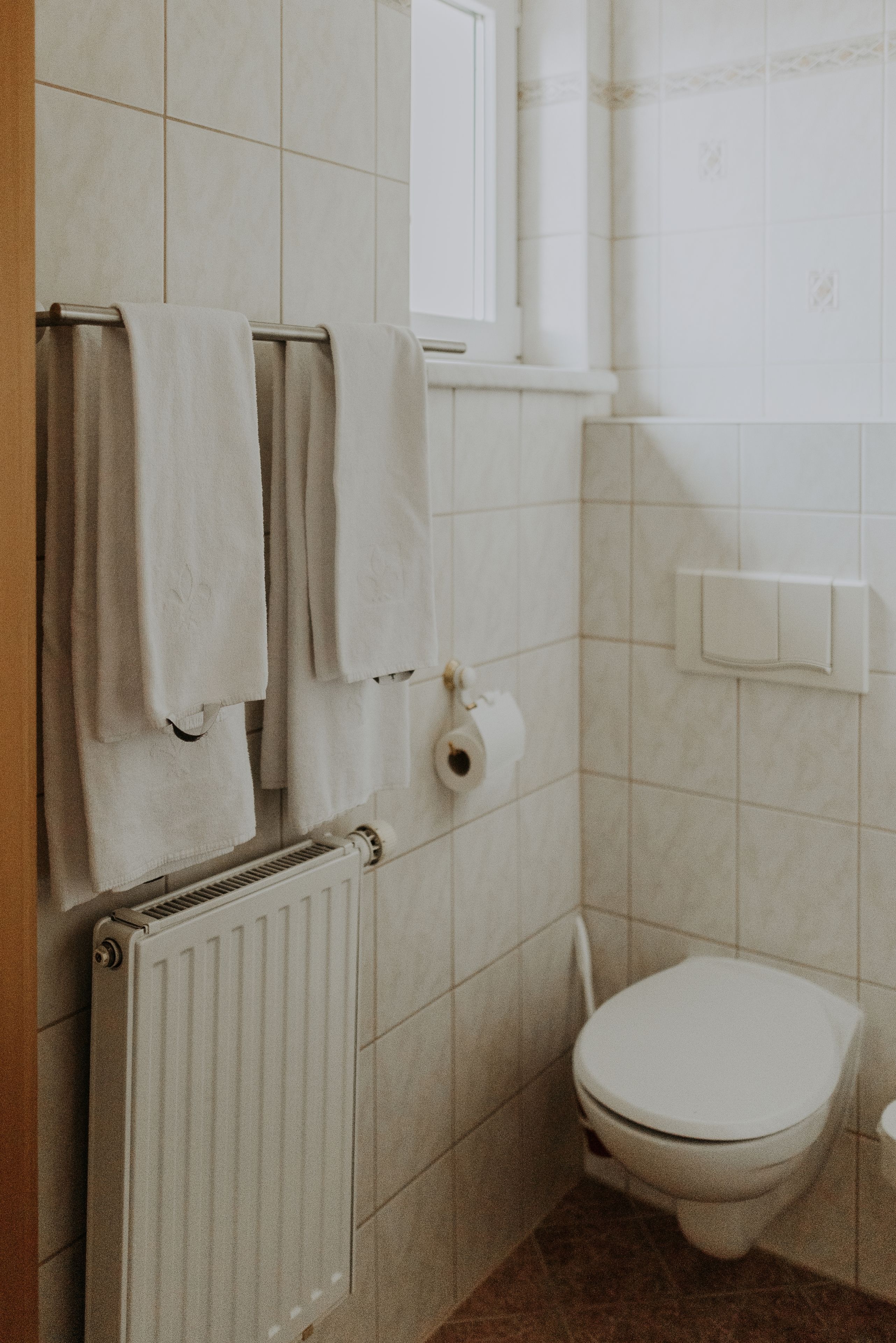 A bathroom with a toilet, a towel rack with towels, a toilet paper holder, and a radiator.