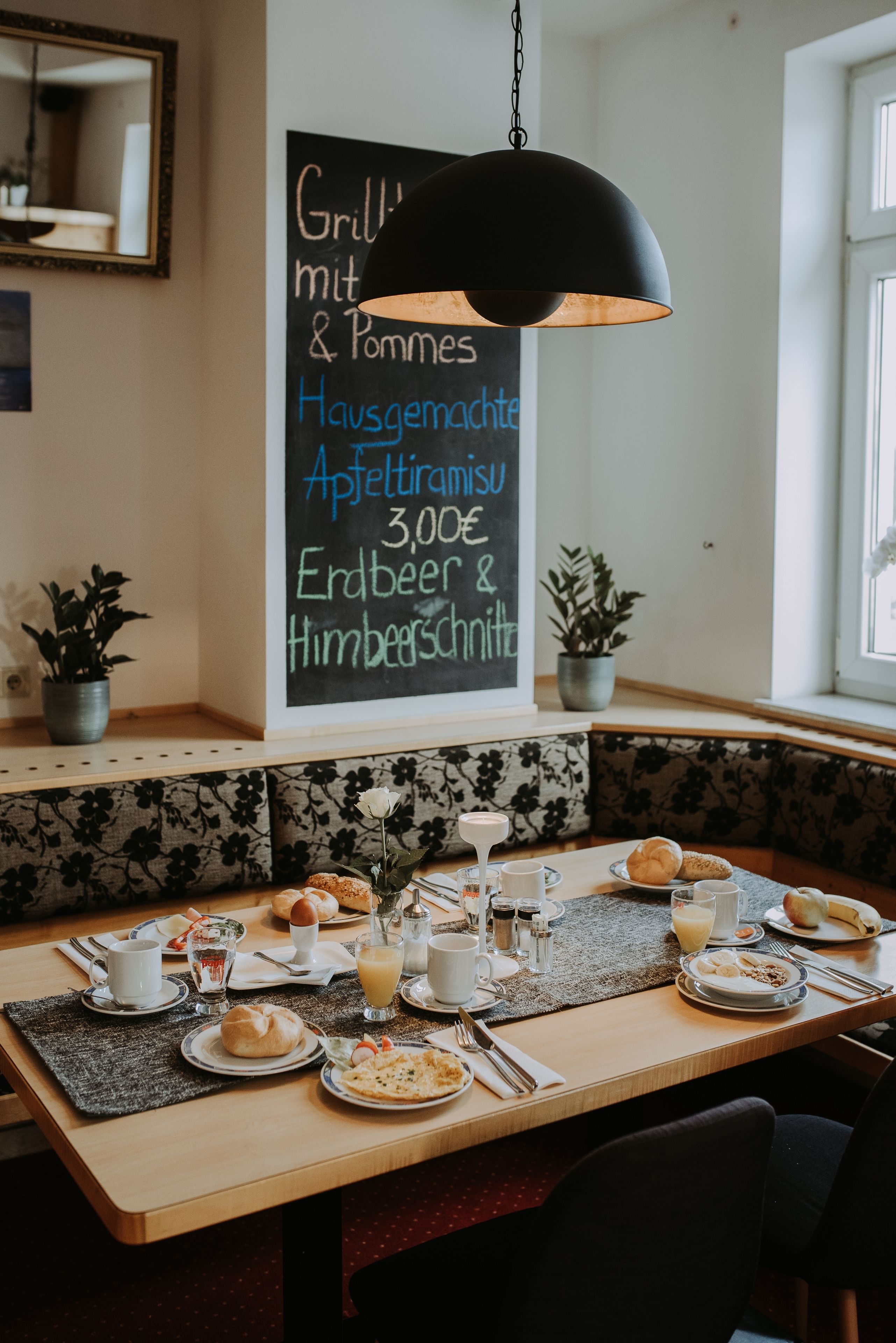 A breakfast setting with a table set for two, featuring plates of food, cups, and a chalkboard menu.