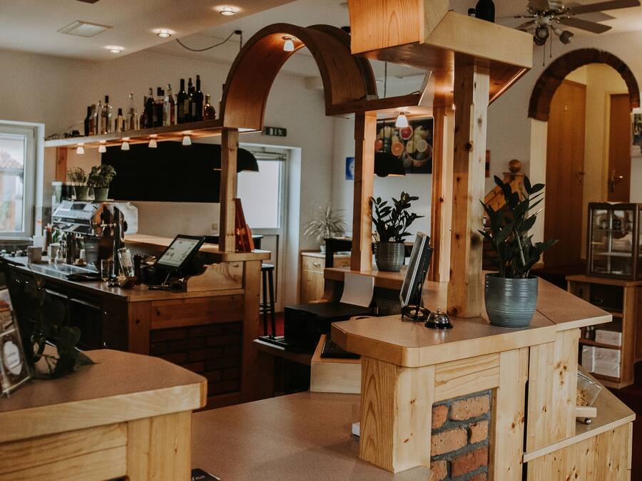 A bar area with wooden furniture and brick accents, featuring a counter, seating, and a ceiling fan.