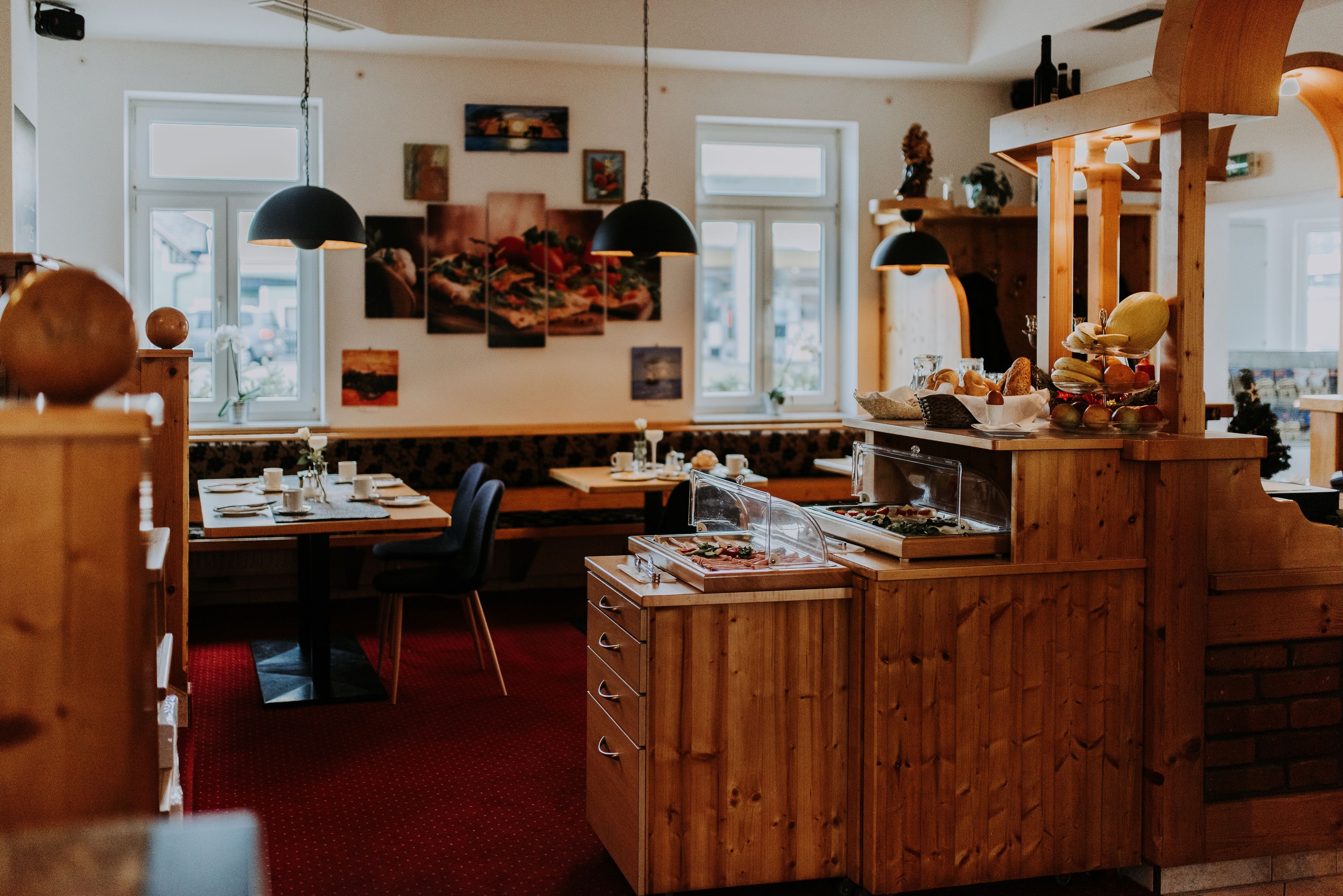 Un restaurante acogedor con muebles de madera, una barra con exhibición de comida y obras de arte en las paredes.