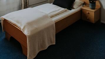 Uma cama de solteiro com cabeceira de madeira, uma mesa de cabeceira com abajur, um quadro na parede e uma janela com cortinas.