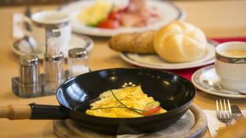 A breakfast setting with an omelette in a pan, a croissant, a cup of coffee, and a plate of vegetables.
