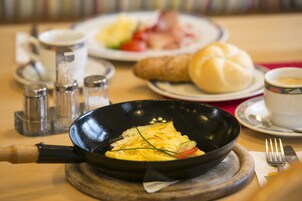 Un desayuno con una tortilla en la sartén, un croissant, una taza de café y un plato de verduras.
