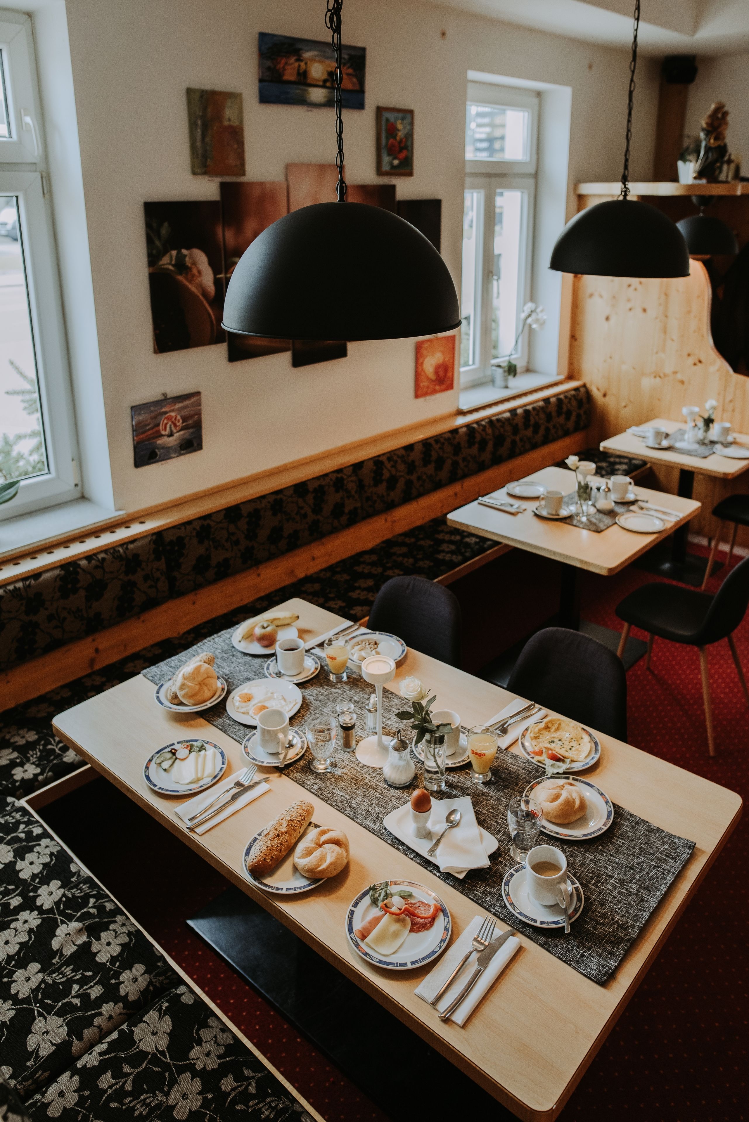 Um restaurante com uma mesa comunitária comprida posta para o café da manhã, cercada por cadeiras e bancos.