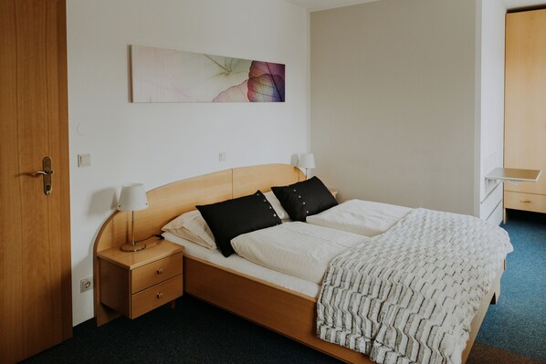 A neatly arranged bedroom with a wooden bed, two bedside tables, a wall-mounted lamp, and a single artwork above the bed. - Gästehaus Feldkirchen (Feldkirchen bei Graz)