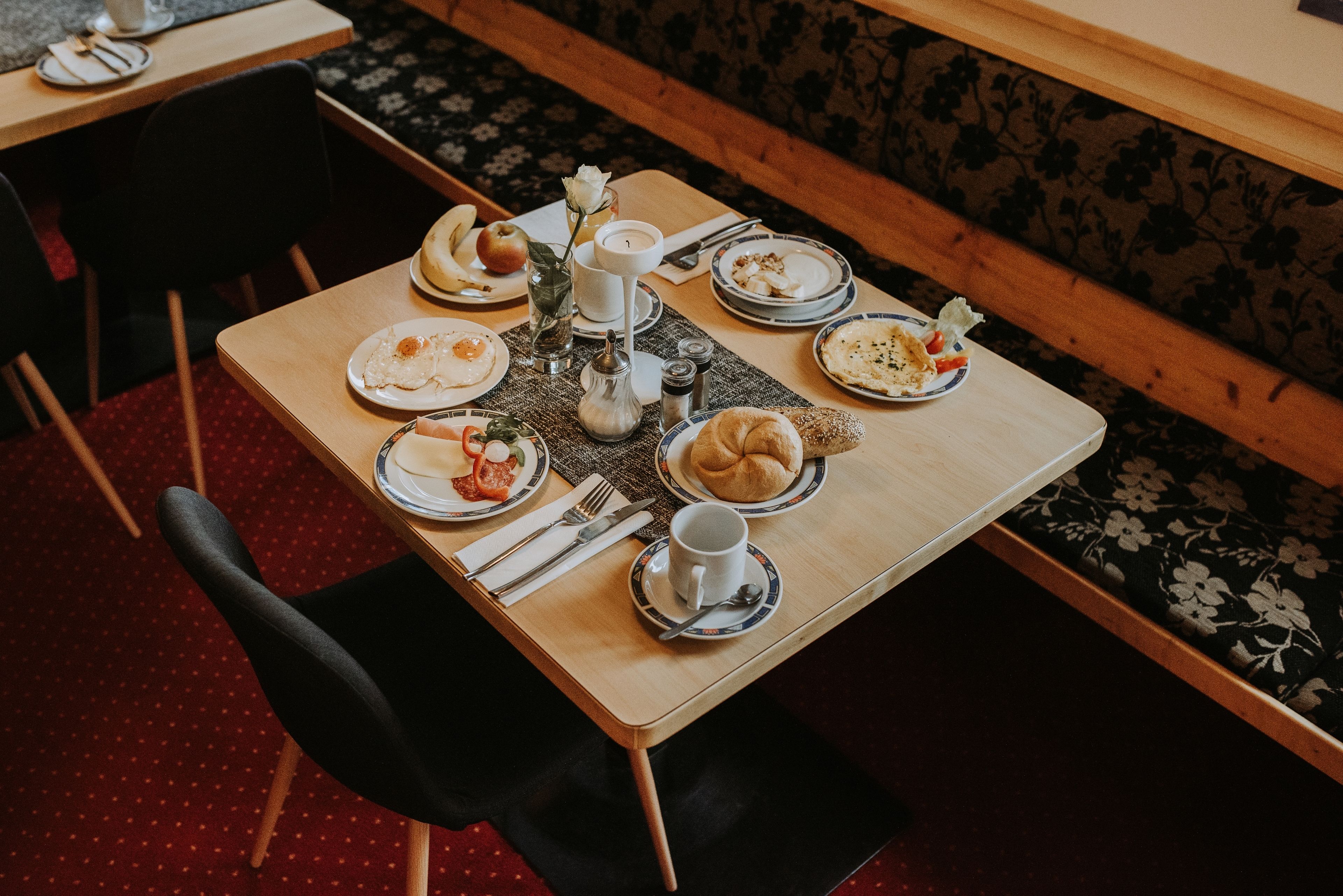 Une table à manger dressée avec des assiettes, des couverts, une bougie et un vase contenant une fleur.