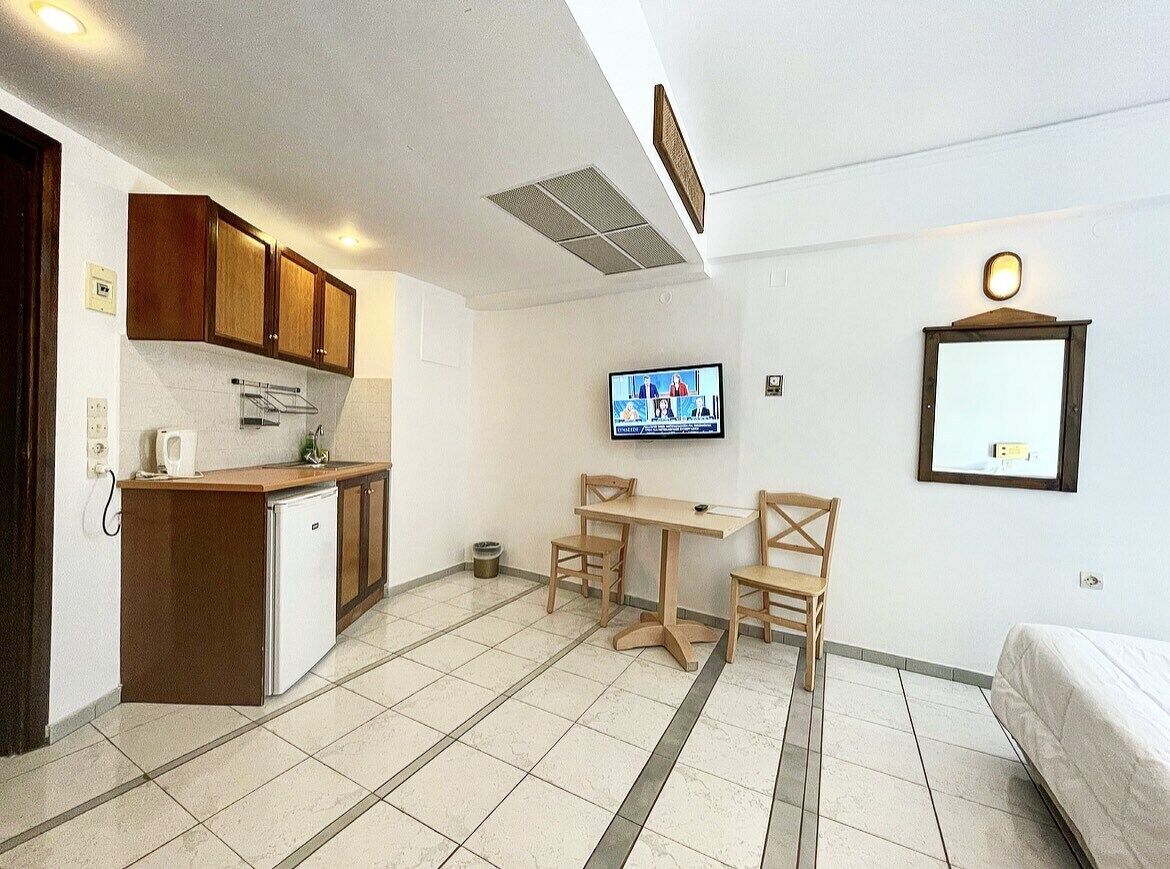 Une pièce compacte comprenant un coin cuisine, un espace repas avec deux chaises, un téléviseur fixé au mur et un lit.