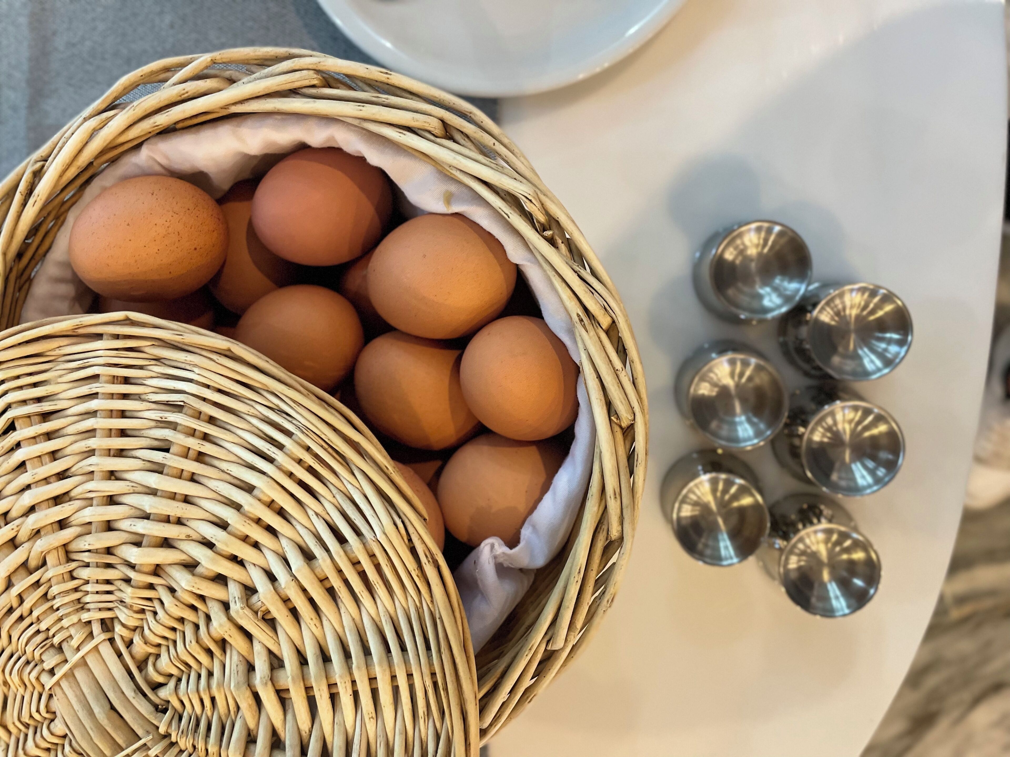 A wicker basket filled with eggs and a white plate with metal lids.