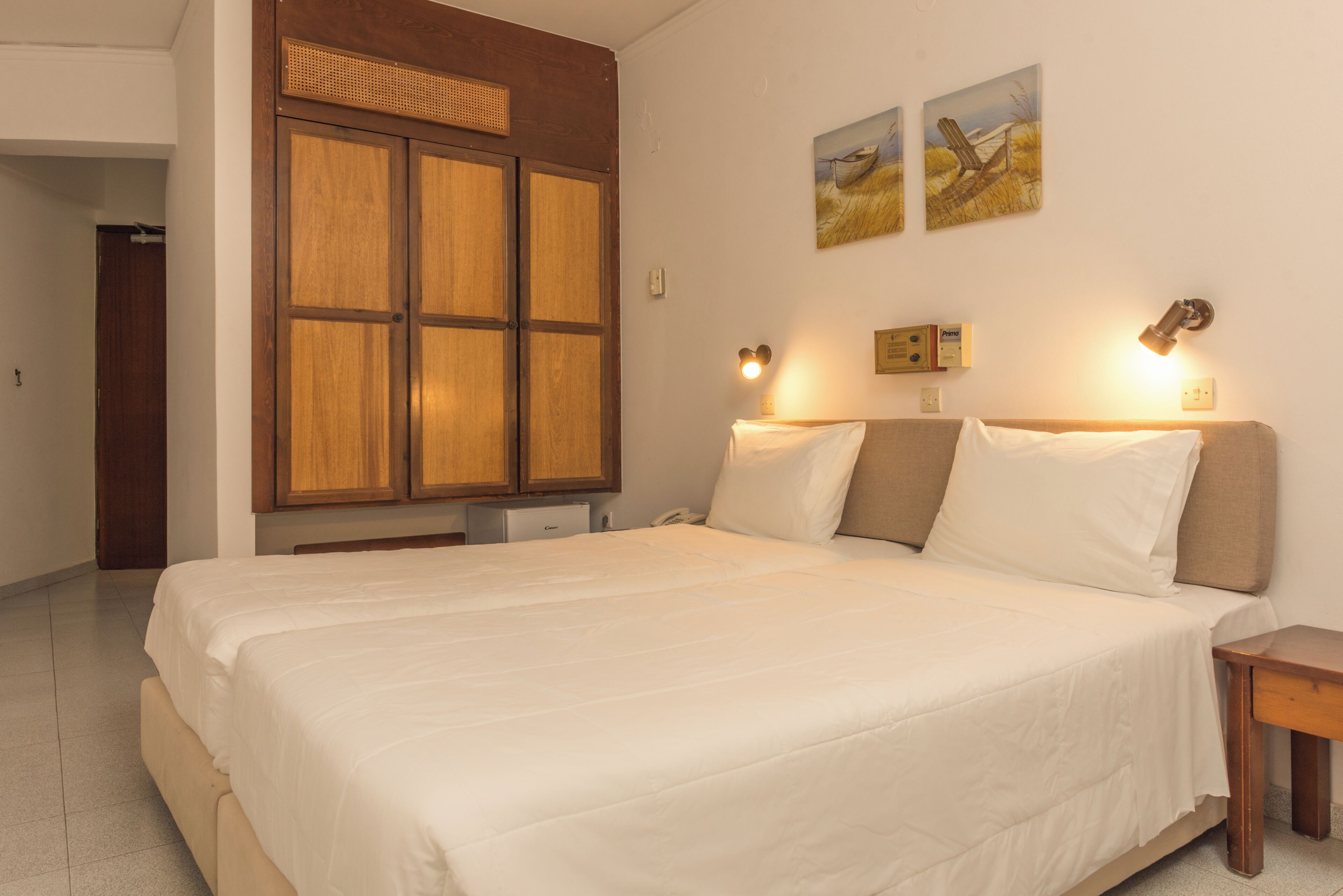 Un dormitorio con una cama grande, un armario de madera, lámparas de noche y dos cuadros en la pared.